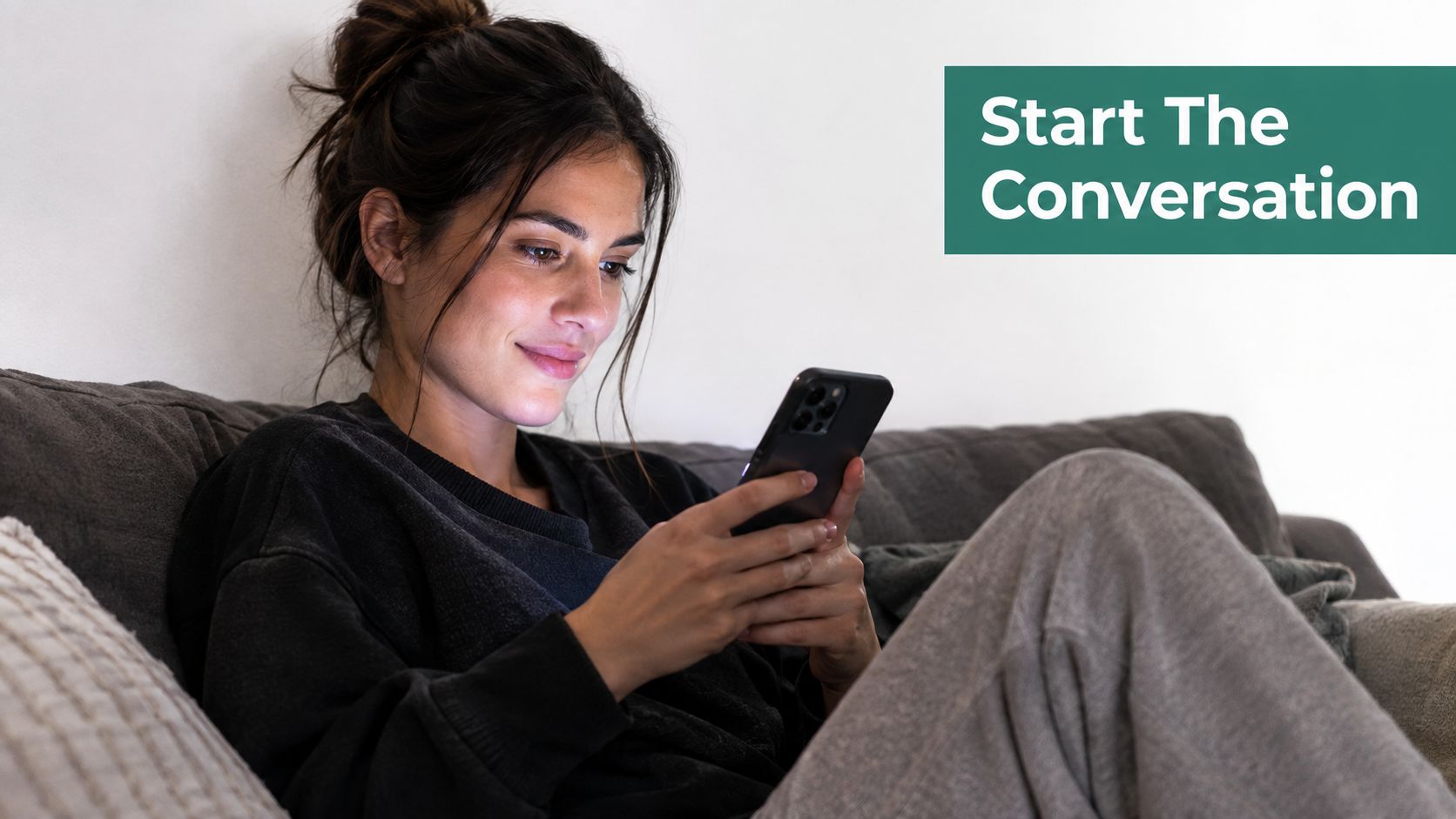 A young woman smiling while sitting on a couch and browsing on her smartphone at home.